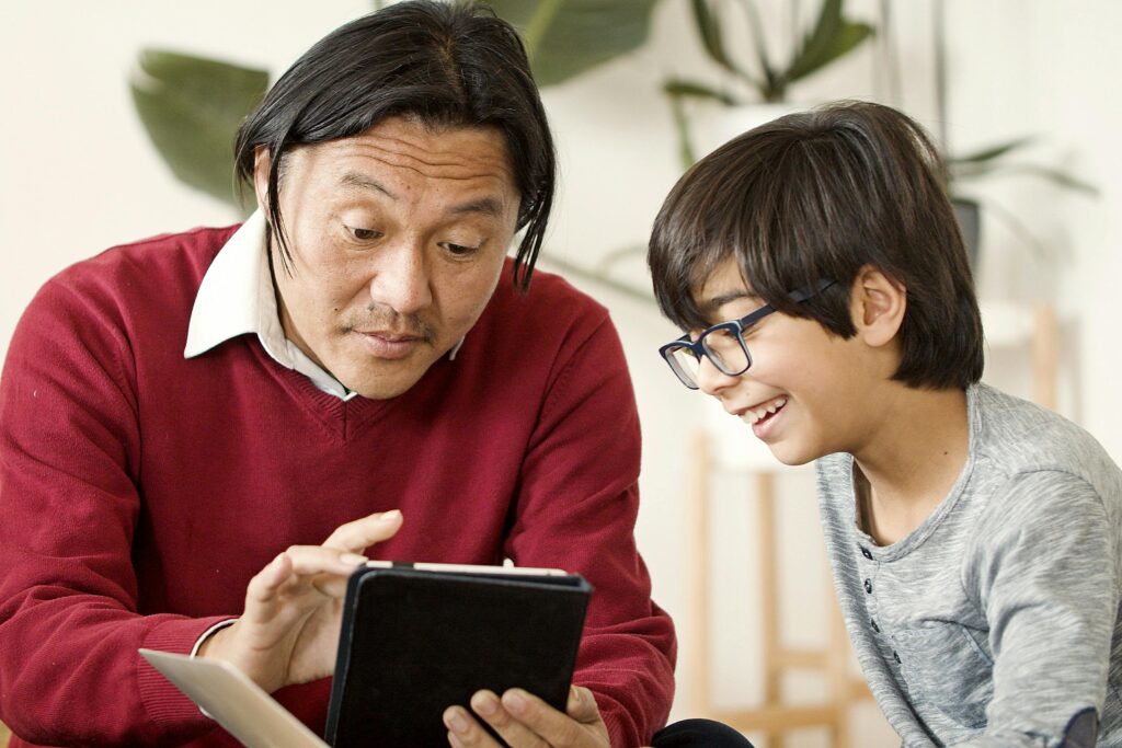 Asian father and child using tablet together in cozy indoor setting.